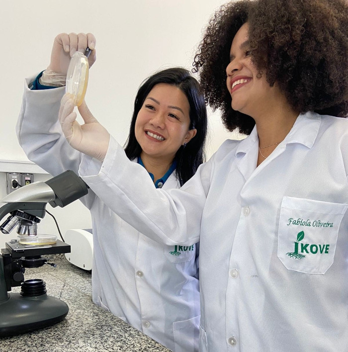 Pesquisadora Fabiola Oliveira segurando uma amostra de fungo na placa de petri e a pesquisadora Clarissa Okino do seu lado, segurando uma caneta apontando para a análise do fungo