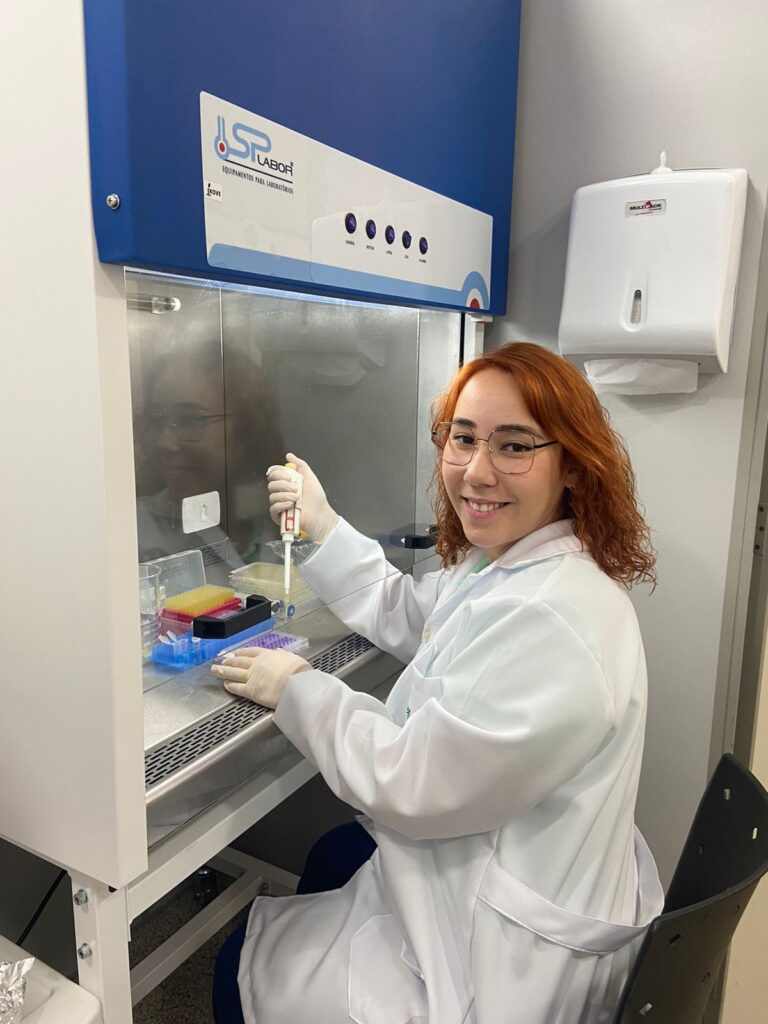 Pesquisadora segurando uma micropipeta, preparando-se para manusear amostras em tubos coloridos sobre a bancada